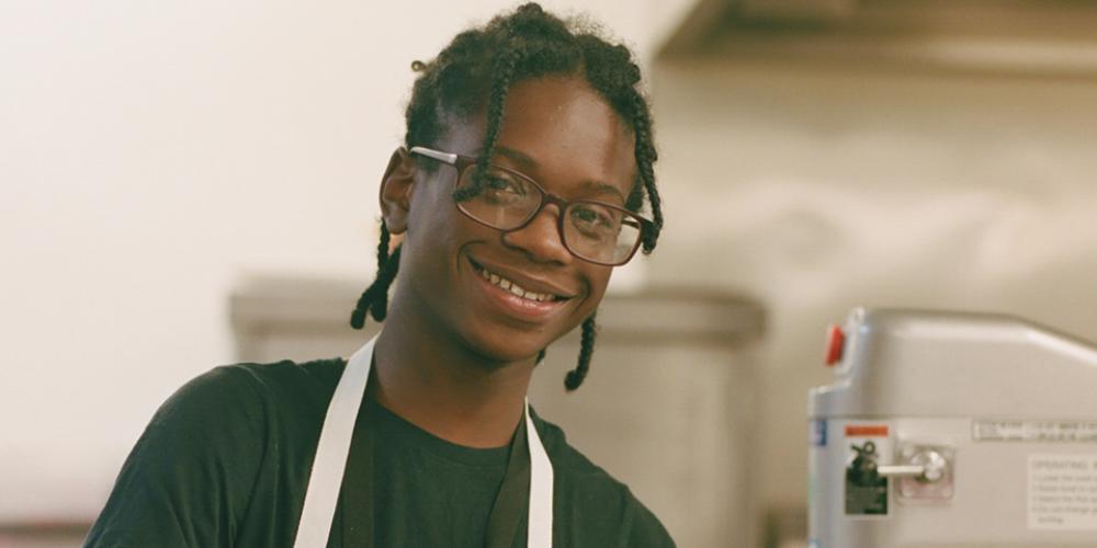 Young Phoenix resident Mikey standing in a kitchen wearing an apron, looking at the camera and smiling.